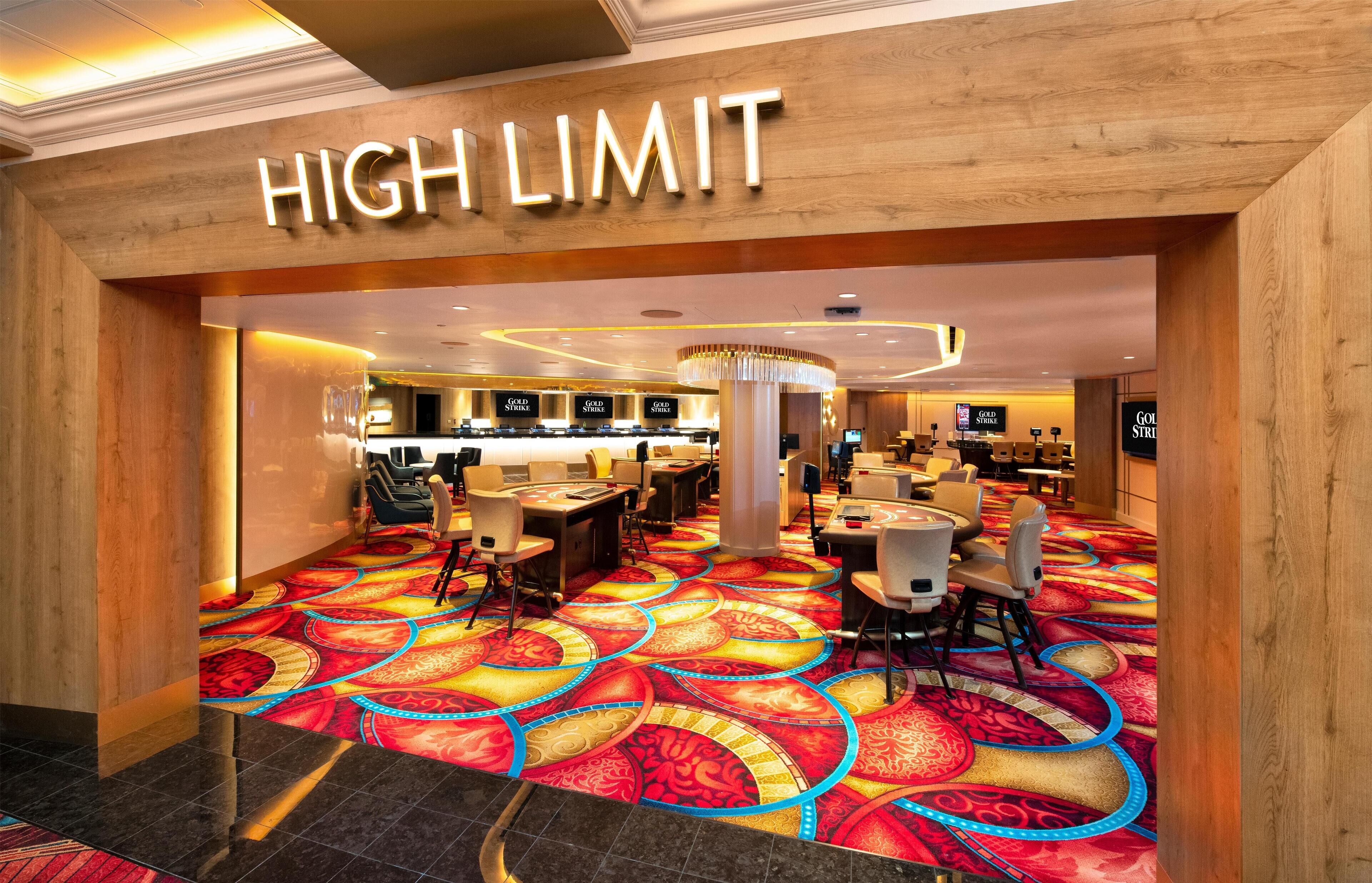 A hotel lobby with a 'HIGH LIMIT' sign, a patterned carpet, and a seating area with tables and chairs.