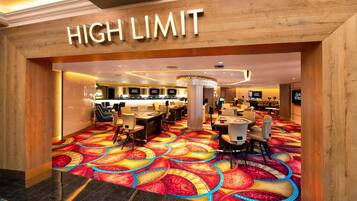A hotel lobby with a 'HIGH LIMIT' sign, a patterned carpet, and a seating area with tables and chairs.