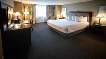 A hotel room with a large bed, a desk with a lamp, a chair, and a bedside table with a lamp.