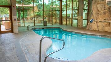 An indoor swimming pool with clear glass walls, a stone wall, and a metal pool ladder.