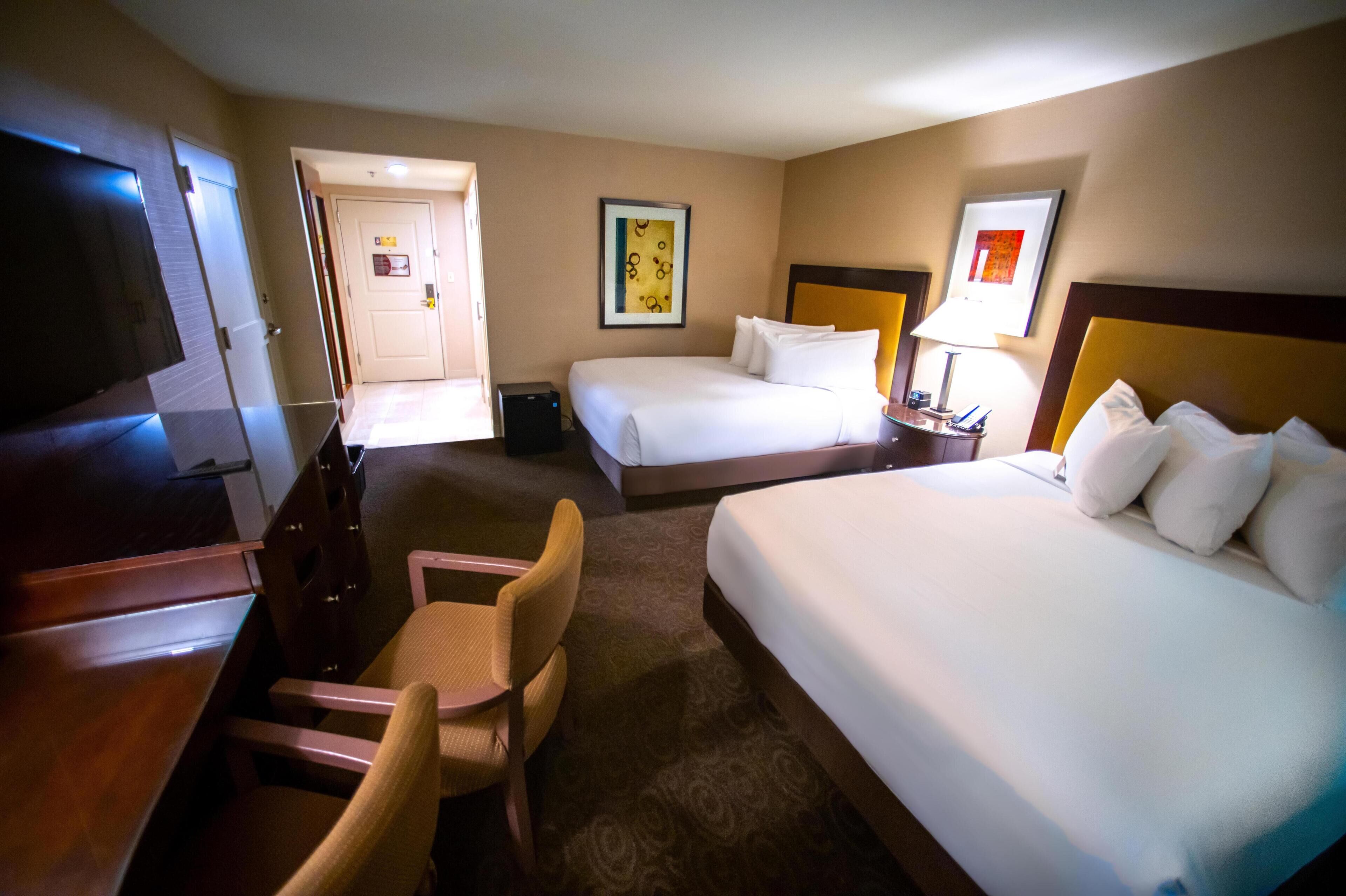 A hotel room with two beds, a desk, a chair, and a television.