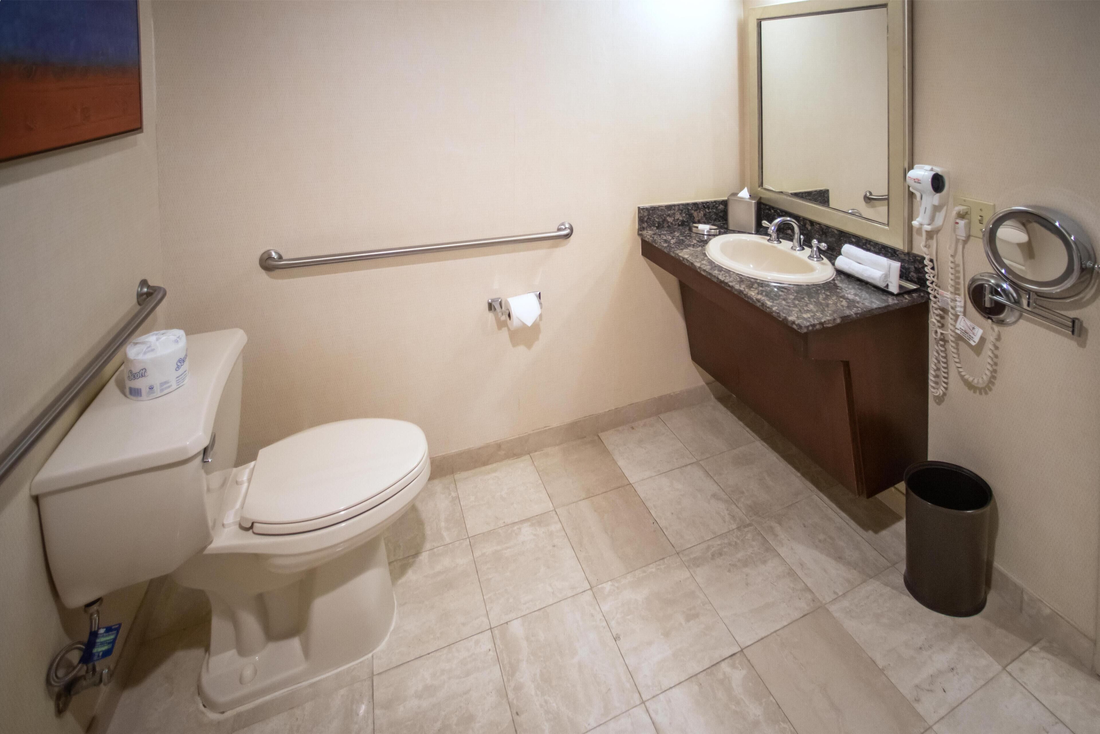 A bathroom with a toilet, sink, mirror, and hand dryer.