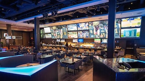 Eine Sportbar mit mehreren Bildschirmen, die Sportereignisse zeigen, Sitzbereichen mit Tischen und Stühlen sowie einer Bar.