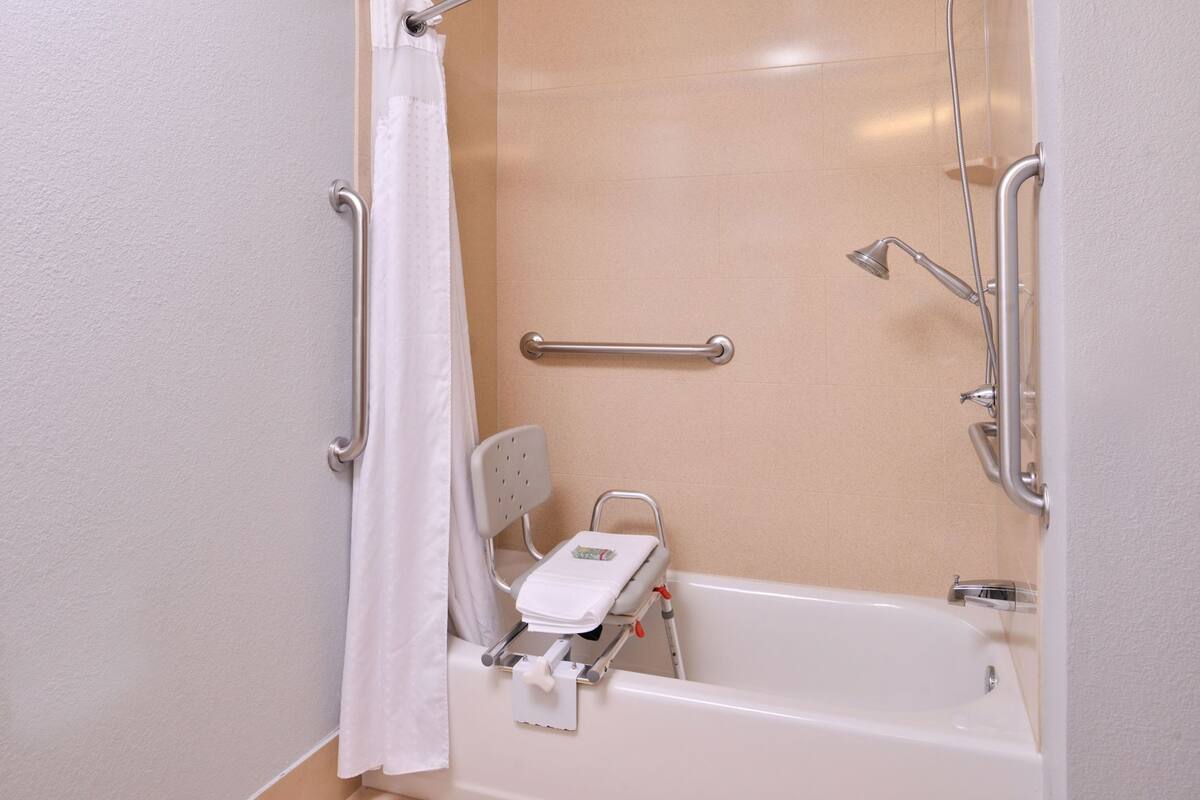 Baño con bañera, ducha, barras de apoyo y asiento accesible para silla de ruedas.