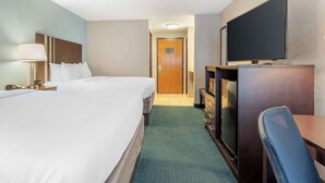 A hotel room with two beds, a desk with a television, a desk lamp, and a carpeted floor.