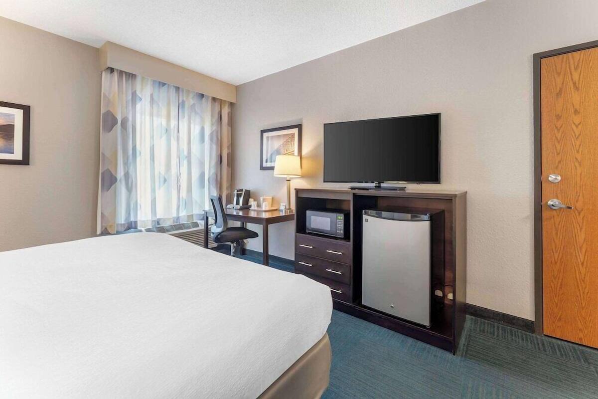 Una habitación de hotel con una cama, un escritorio con computadora, televisor y minibar.