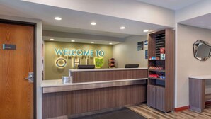 A reception area with a wooden reception desk, a 'Welcome to OHI' sign, a small shelf with snacks, and a mirror on the wall.