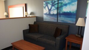 Ein Wohnzimmer mit einer Couch, einem Holztisch, einer Lampe und einem Bild an der Wand.
