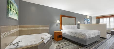 Una habitación de hotel moderna con una cama grande, un baño independiente con bañera y un ventanal que proporciona luz natural.