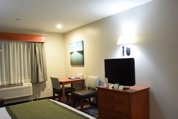 Une chambre d’hôtel avec un lit, un bureau et une chaise, une télévision, une lampe et un tableau au mur.