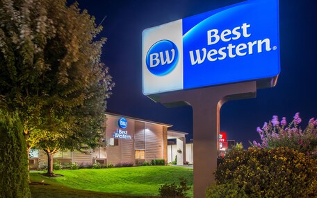 A Best Western hotel sign with a logo, a well-lit building, and a landscaped lawn.