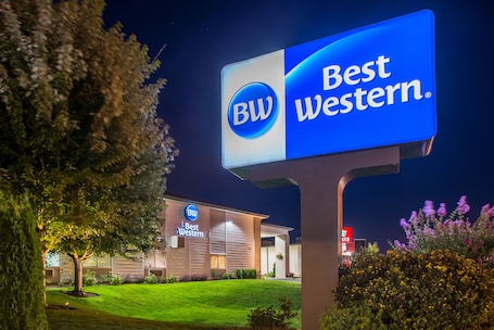 A Best Western hotel sign with a logo, a well-lit building, and a landscaped lawn.