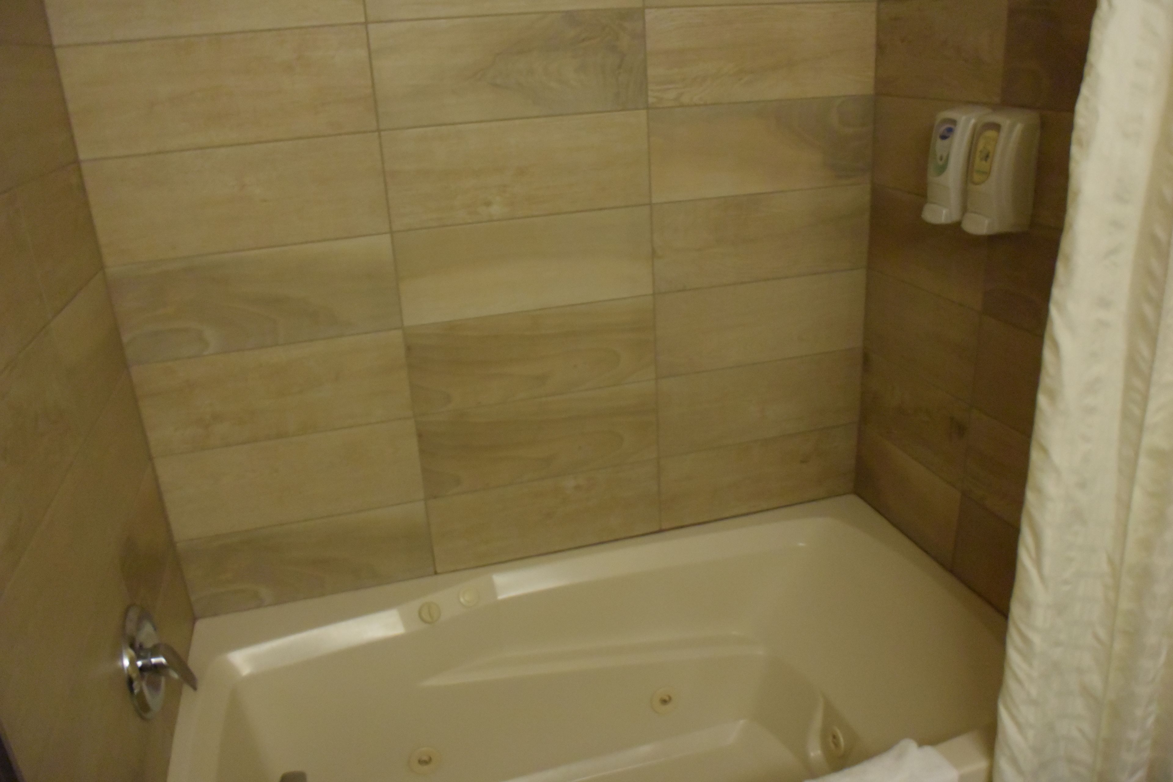 Un baño con bañera, paredes de azulejos y dispensador de jabón.