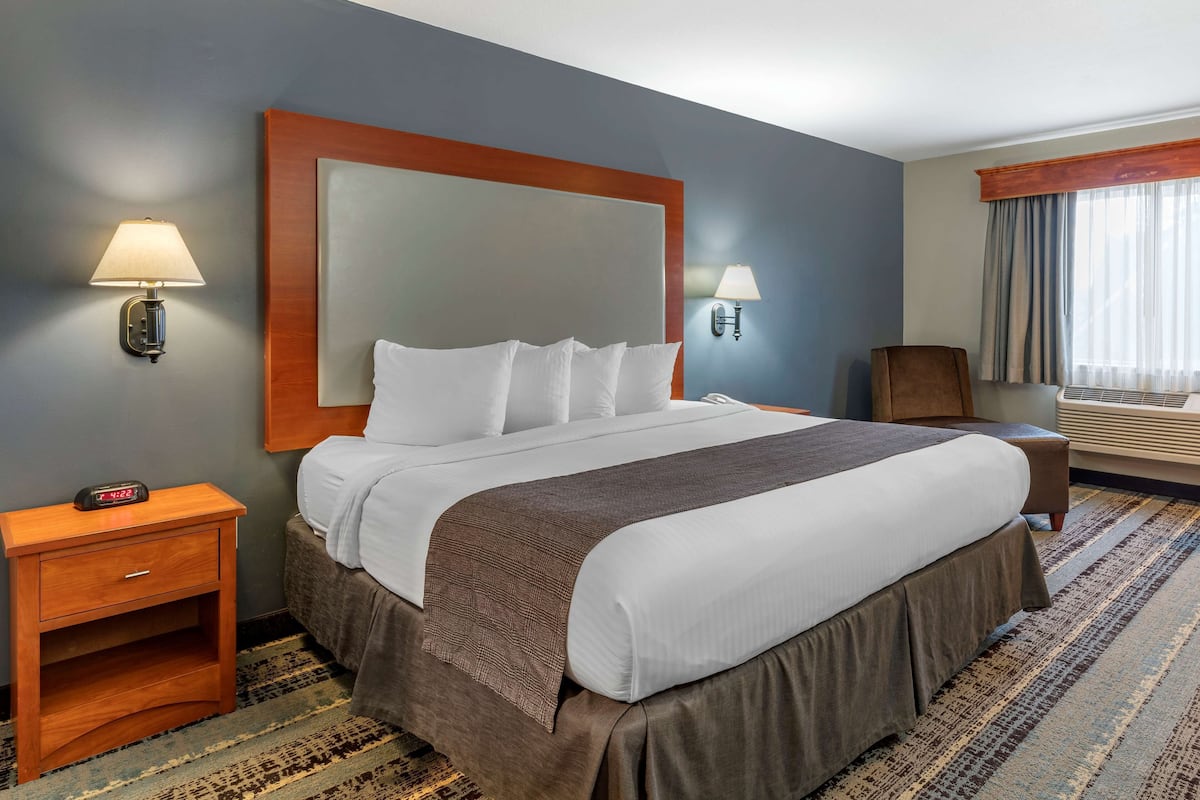A hotel room with a large bed, two bedside lamps, a nightstand, a chair, and a window with curtains.