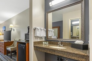 A hotel bathroom with a granite countertop sink, a large mirror, a towel rack, a chair, a television, and a coffee machine. - Best Western Newberg Inn (Newberg)