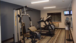 Ein Fitnessraum mit Cardiogeräten, einer Gewichtbank und einem an der Wand montierten Fernseher.