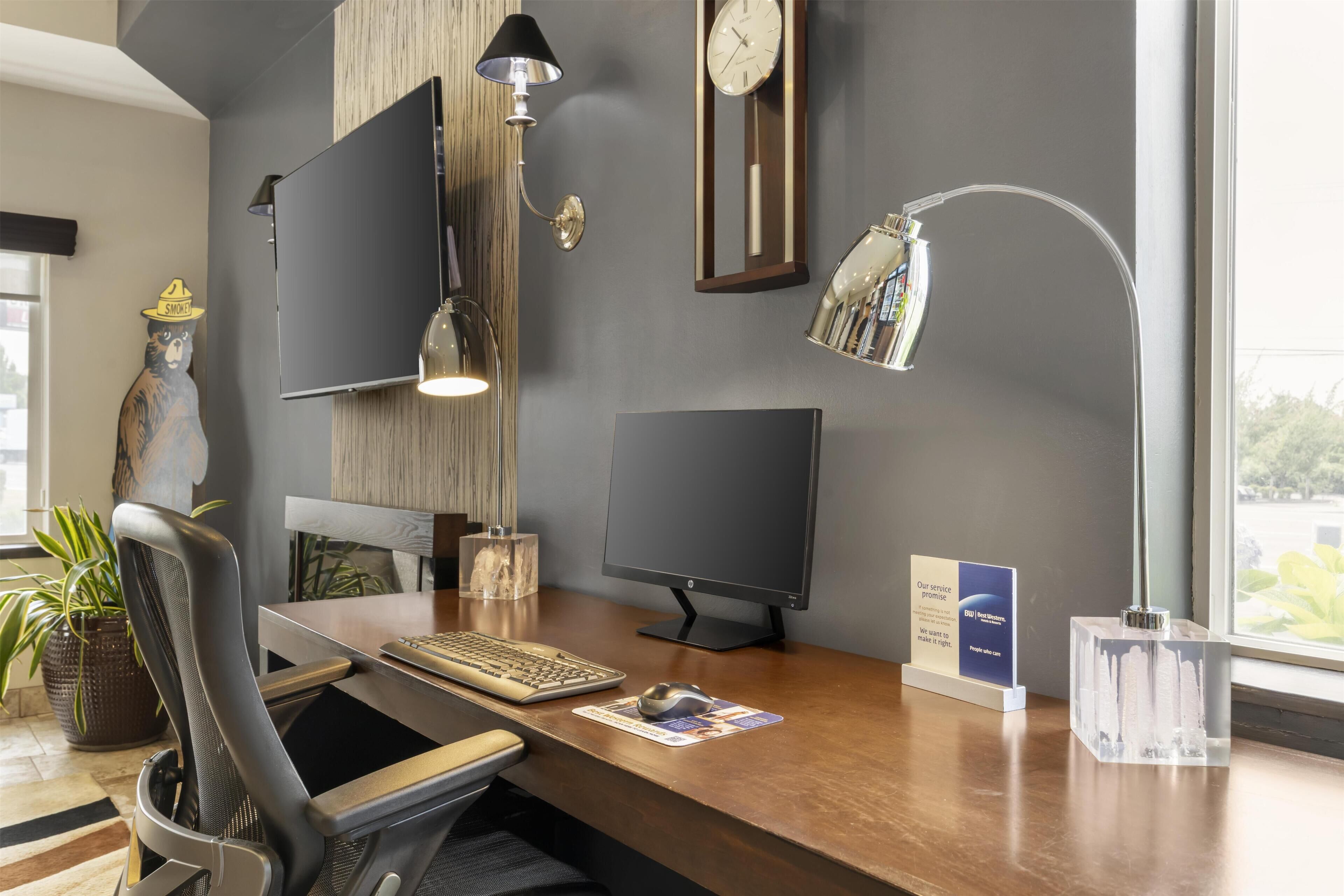 Et moderne skrivebord med en computer, tastatur og mus. Der er en stol, en lampe og et ur på væggen.