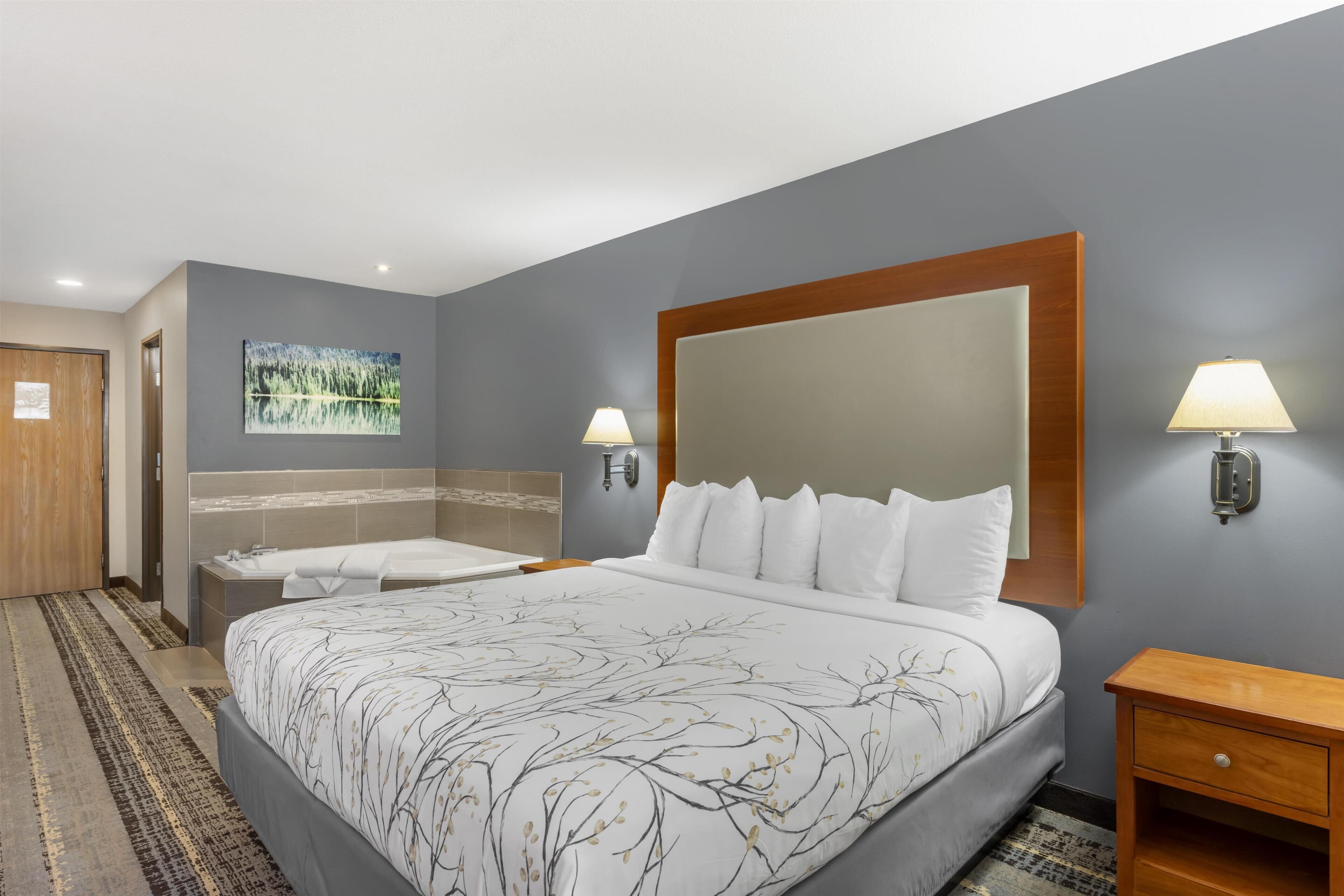 A hotel room with a large bed, a bathroom with a bathtub, and a painting on the wall.