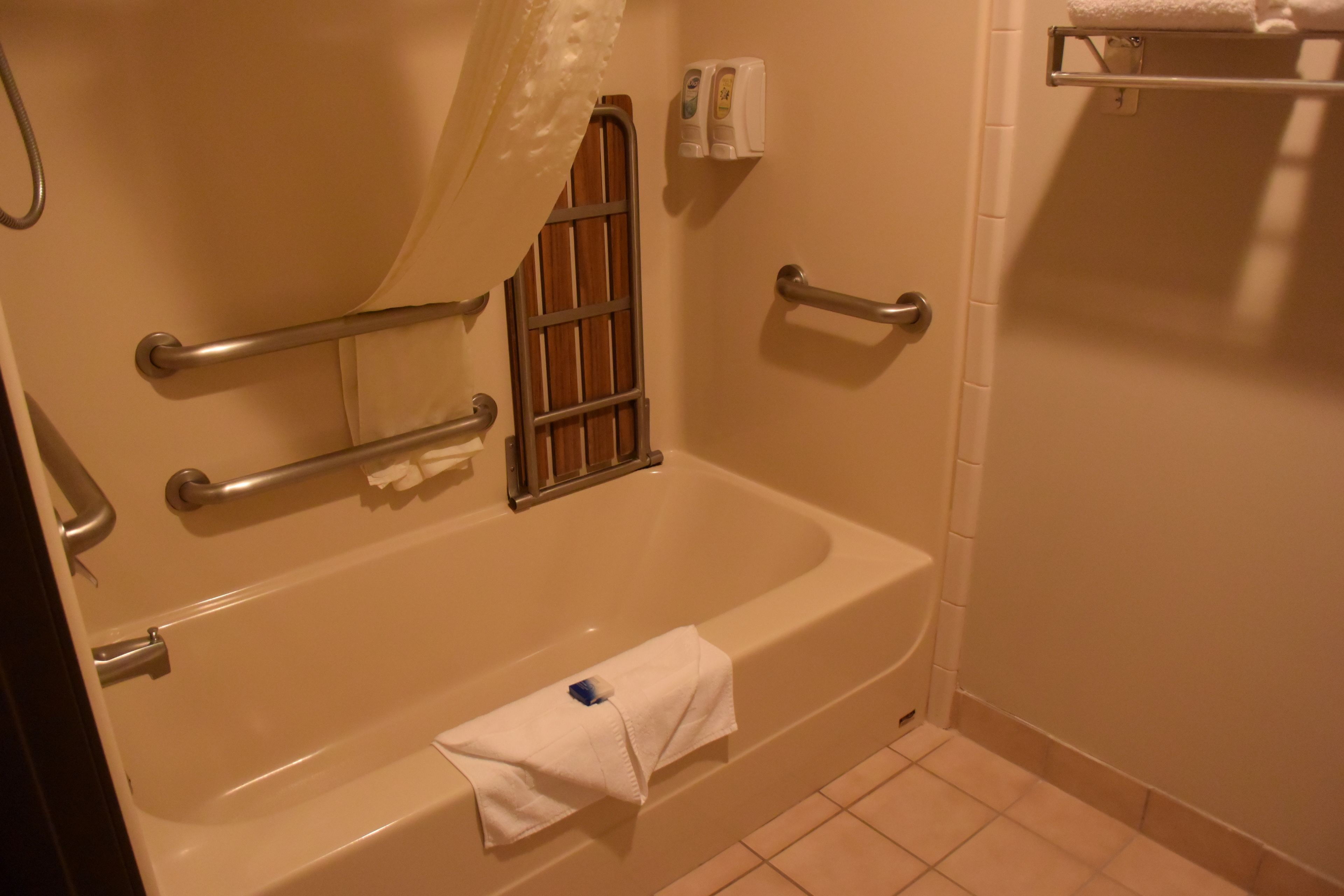 A bathroom with a bathtub, grab bars, a shower curtain, and a towel rack.