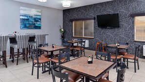 Ein Restaurant mit mehreren Tischen und Stühlen, einem an der Wand montierten Flachbildfernseher und einem großen abstrakten Gemälde.