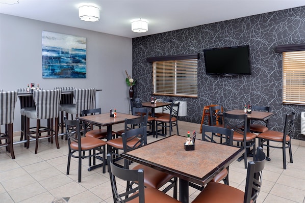 Un restaurante con varias mesas y sillas, un televisor de pantalla plana montado en la pared y un cuadro abstracto grande en la pared.