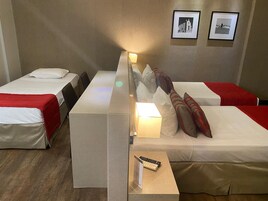 Camera d'albergo con due letti, un comodino con una lampada, un telecomando e due quadri appesi al muro.