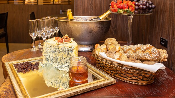 Uma mesa com uma garrafa de champanhe, uma cesta de frutas, um prato de queijos e uma cesta de pão.