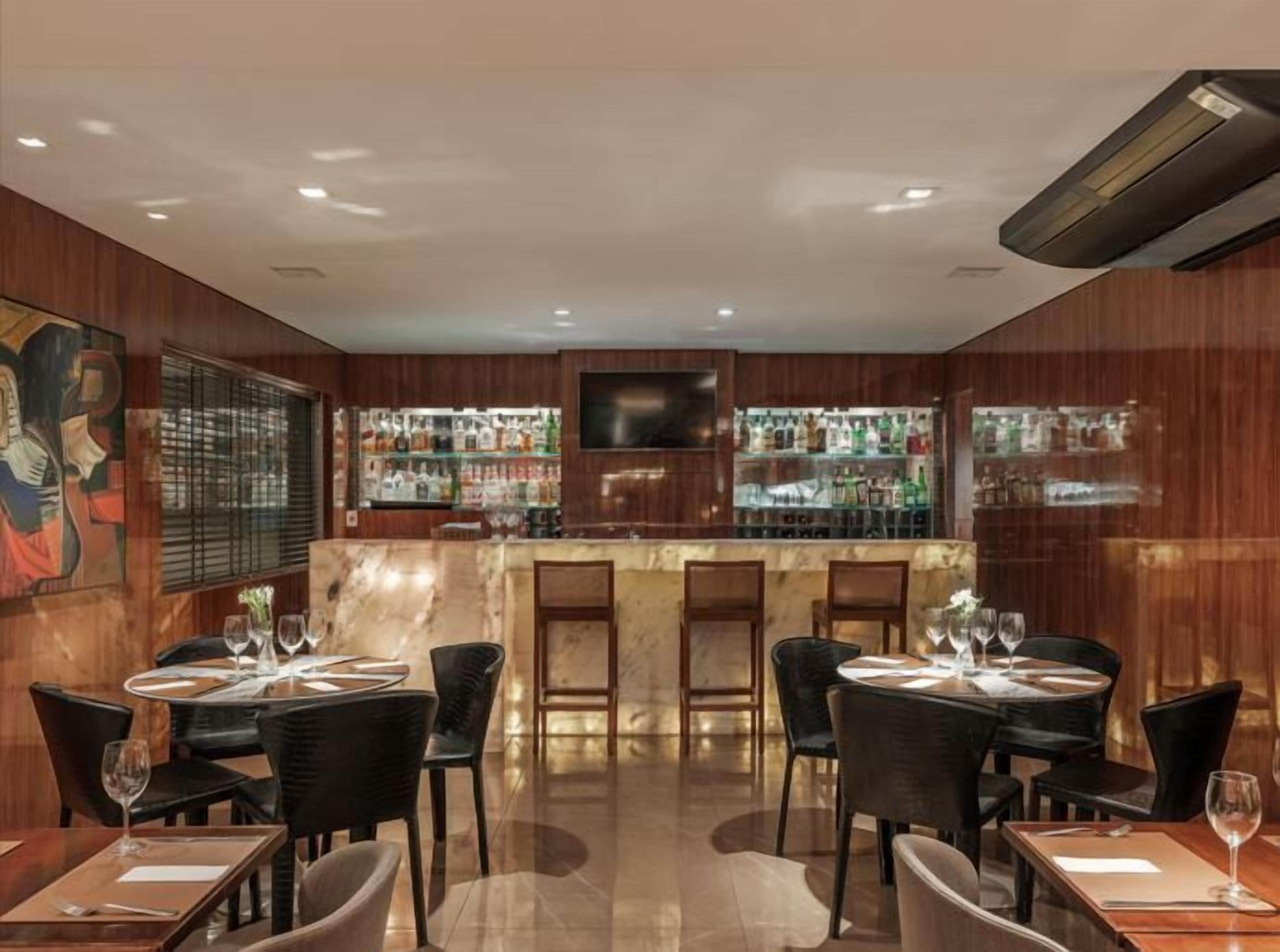 Een restaurant met een bar, houten lambrisering en een groot schilderij aan de muur.