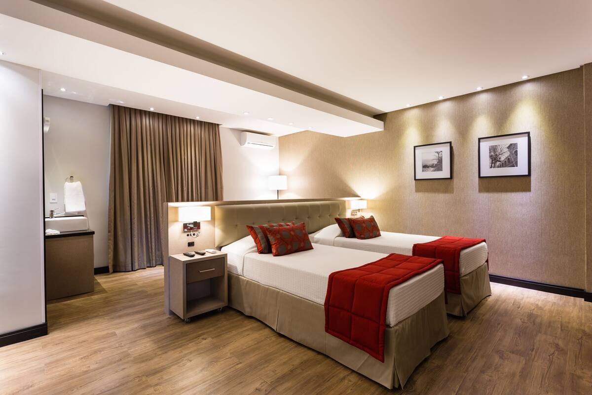 Ein Hotelzimmer mit zwei Betten, einem Schreibtisch, einem Stuhl, einer Lampe und einer Wand-Klimaanlage.