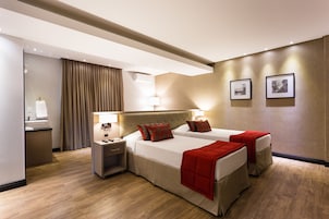 Camera d'albergo con due letti, una scrivania, una sedia, una lampada e un condizionatore d'aria a muro.