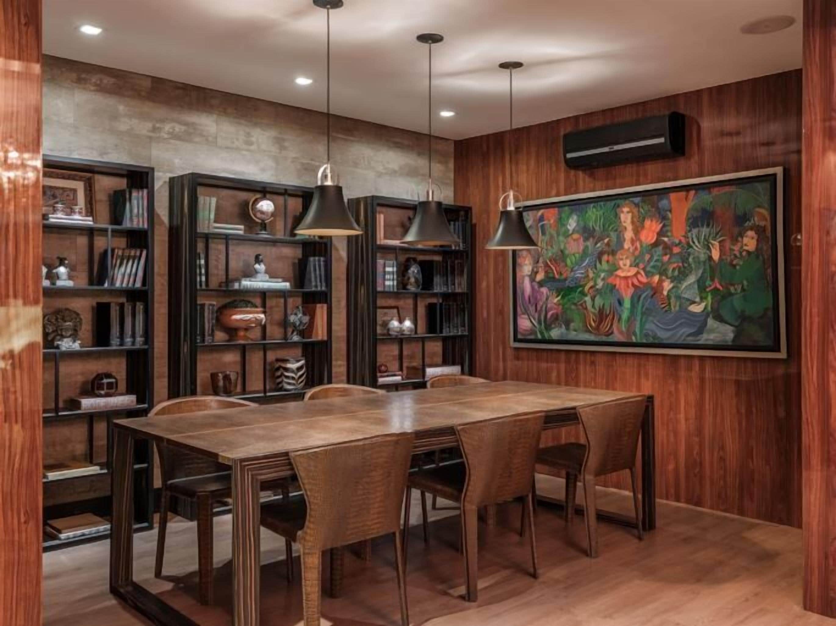 A dining area with a wooden table and chairs, surrounded by bookshelves and a large painting.
