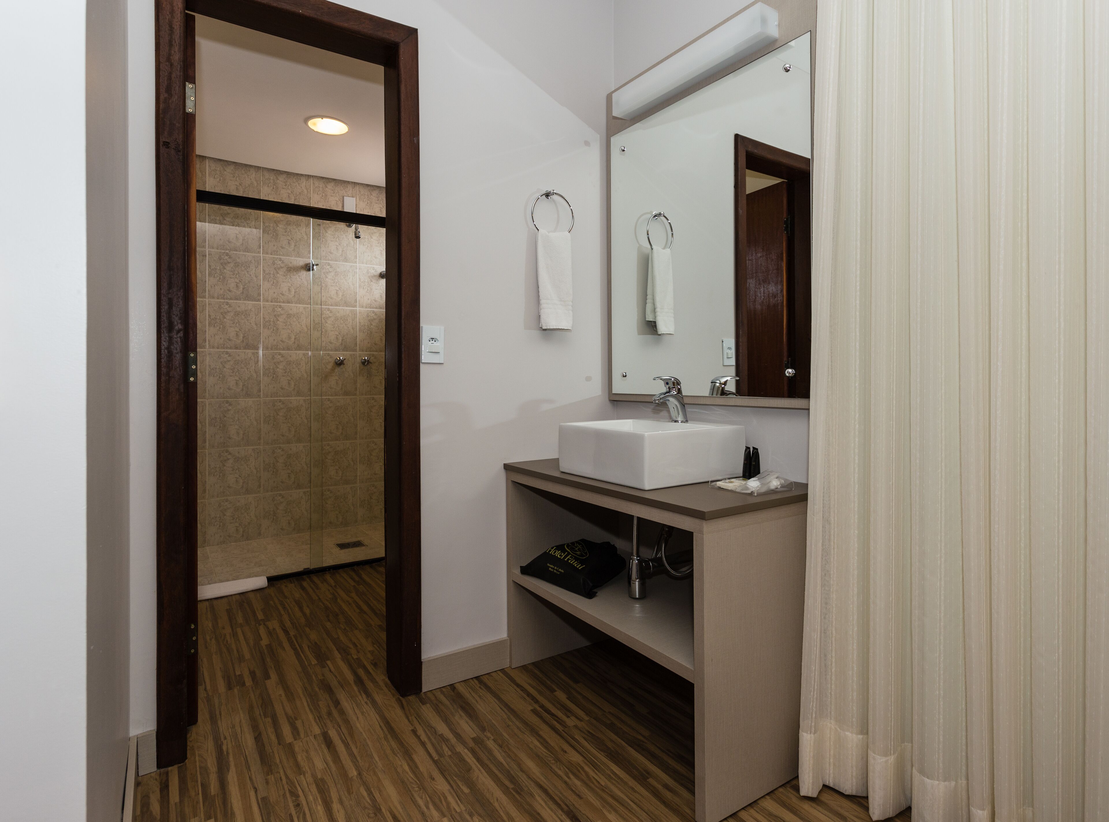 A bathroom with a shower, a sink, a mirror, and a towel rack.