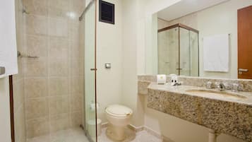 Un baño con ducha de vidrio, inodoro, lavabo con encimera de mármol y un espejo grande.