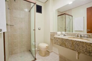 Un baño con ducha de vidrio, inodoro, lavabo con encimera de mármol y un espejo grande.