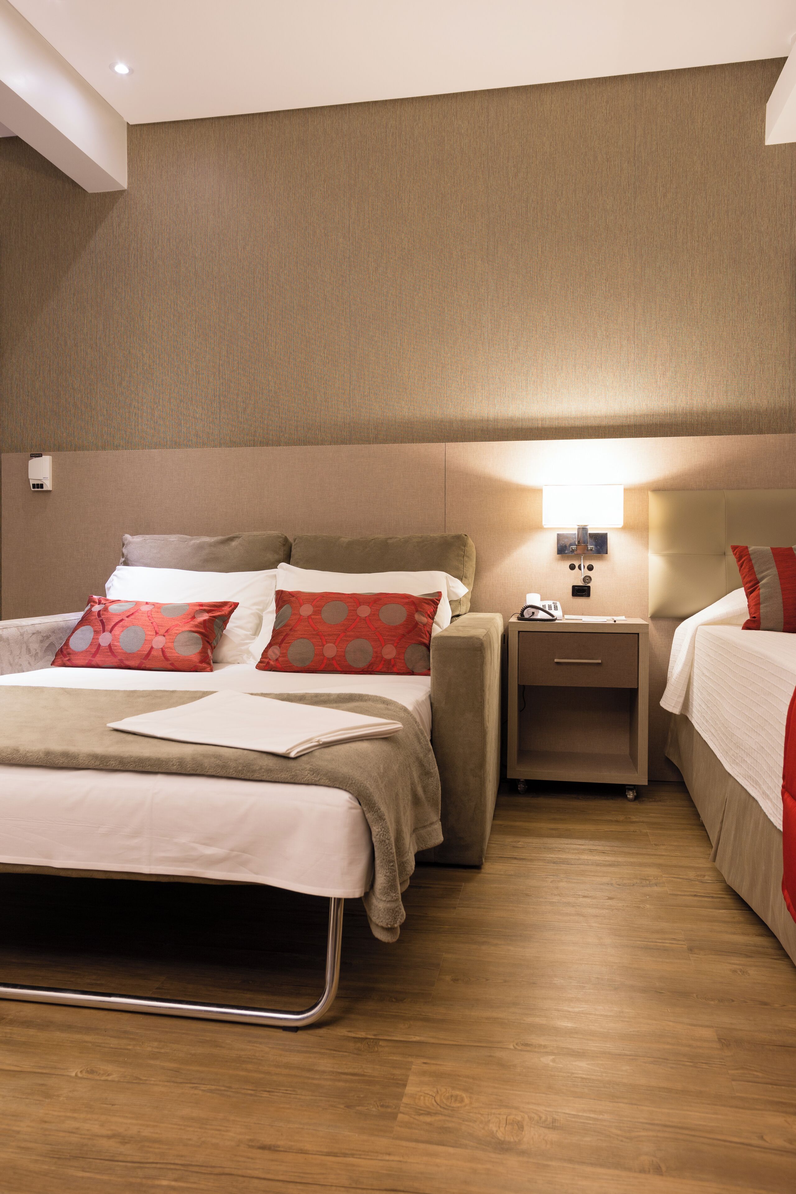 Una habitación de hotel con una cama grande, dos mesitas de noche y una mesita auxiliar con una lámpara.