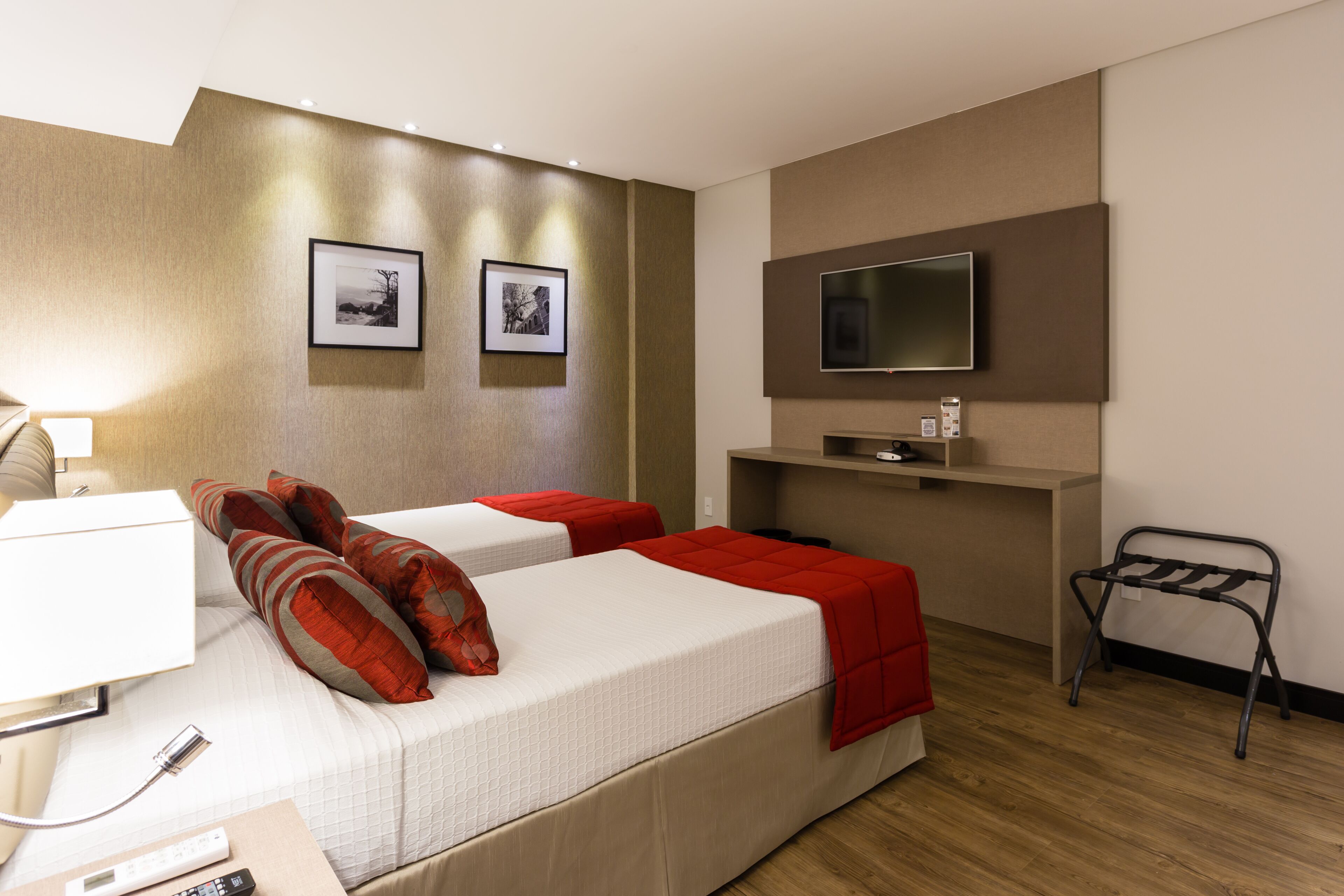 A hotel room with two beds, a TV, a desk with a lamp, and a small table.