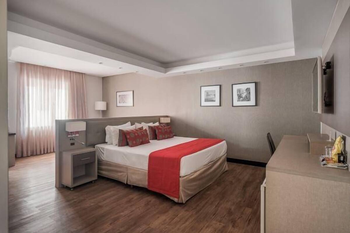 Ein modernes Hotelzimmer mit einem großen Bett, Nachttischen, einem Schreibtisch und einem Flachbildfernseher.