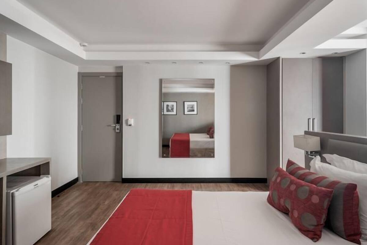 Ein modernes Hotelzimmer mit Bett, Schreibtisch, Spiegel und einem roten Teppich.