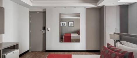 Una camera d'albergo moderna con un letto, una scrivania, uno specchio e un tappeto rosso.