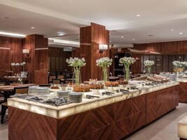 A modern hotel lobby with a central island featuring a buffet setup, wooden paneling, and ambient lighting.