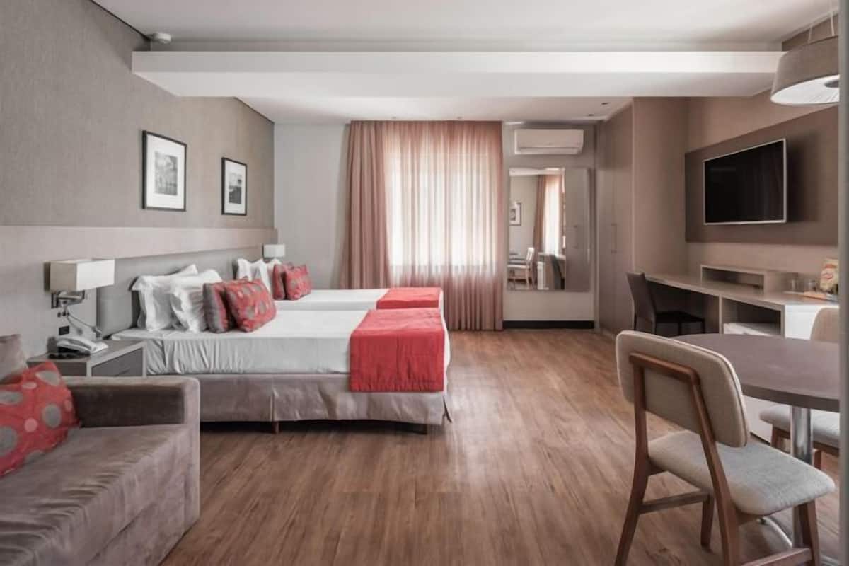 Ein Hotelzimmer mit zwei Betten, einem Schreibtisch, einem Sessel, einem Fernseher und einem Spiegel.