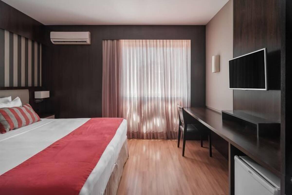 Ein modernes Hotelzimmer mit Bett, Schreibtisch, Fernseher und einem Fenster mit Vorhängen.
