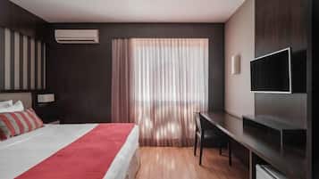 A modern hotel room with a bed, a desk, a TV, and a window with curtains.