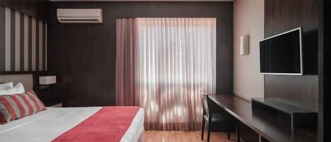 A modern hotel room with a bed, a desk, a TV, and a window with curtains.