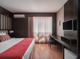 Una camera d'albergo moderna con un letto, una scrivania, una TV e una finestra con tende.