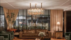 Uma sala de estar moderna com sofá de couro, mesa de centro redonda, lustre e uma grande janela com persianas.