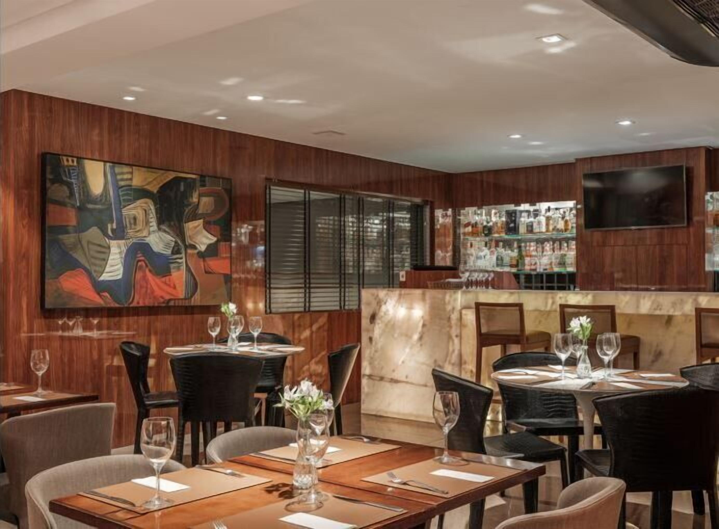 Een restaurant met houten lambrisering, een bar en een groot schilderij aan de muur.