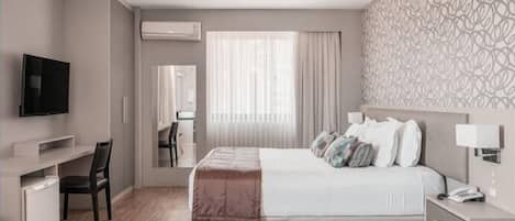 A hotel room with a bed, bedside table, desk, chair, TV, air conditioning unit, window with curtains, and a patterned wall.