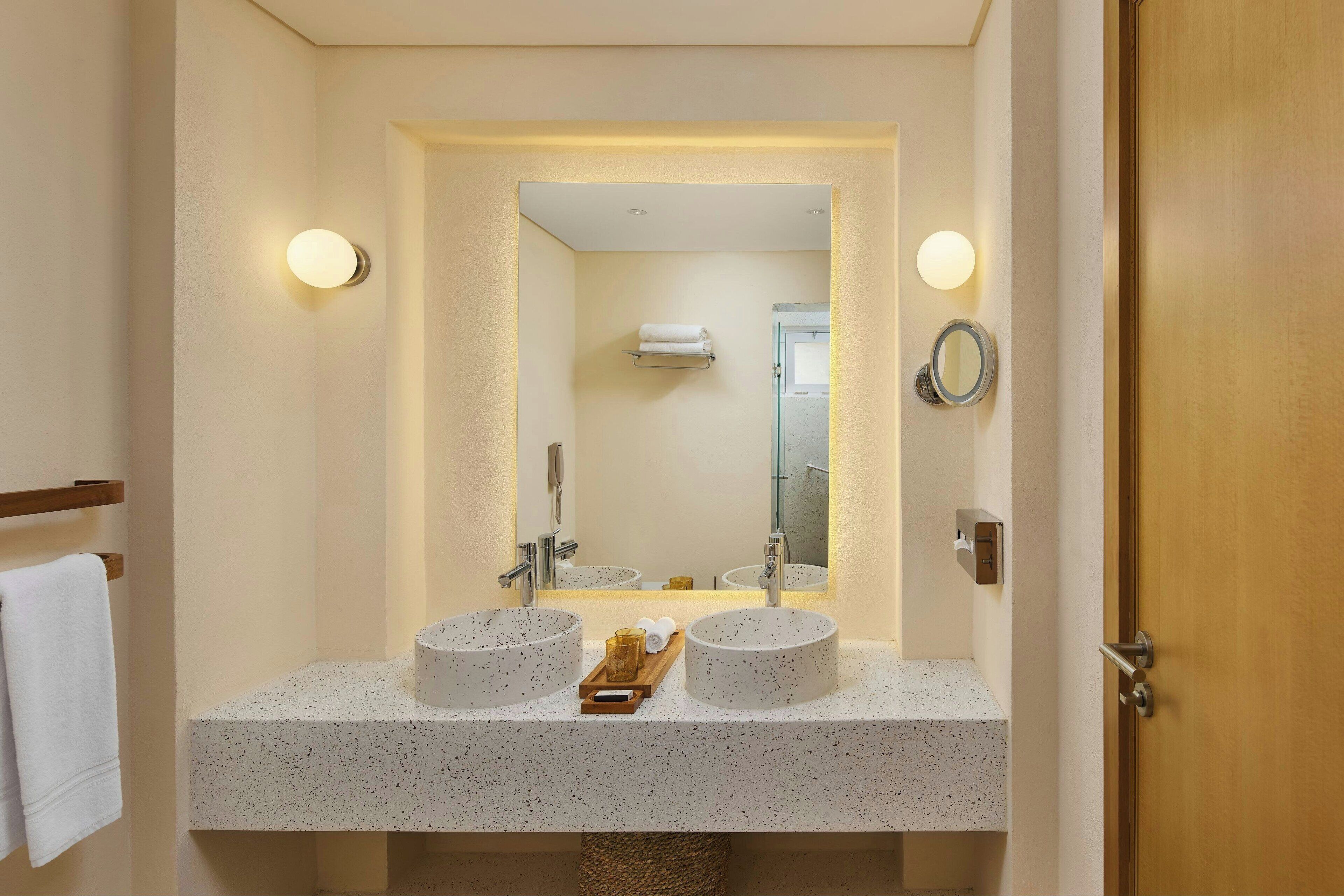 Un baño con dos lavamanos redondos, un espejo y un perchero para toallas.