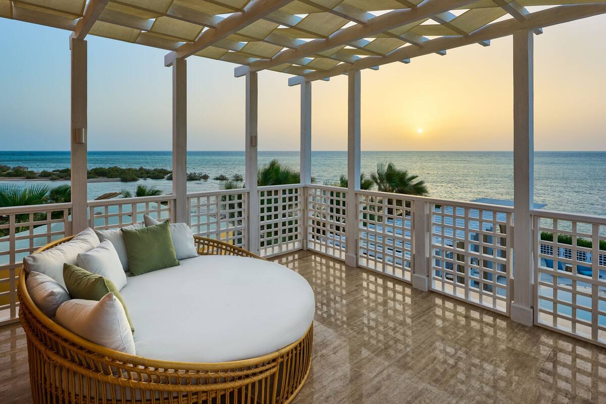 A covered outdoor seating area with a view of the sea at sunset.